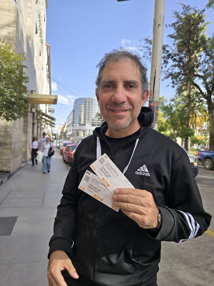 Hincha sonriendo en la vereda con sus dos entradas recién entregadas